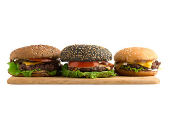 Three burgers on a wooden board cut out on a white background. Beef patties, cheddar cheese, lettuce, bacon, pickled cucumber, tomato and balsamic burgers. In the background are two burgers.