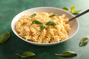 Plate with tasty macaroni and basil on color background