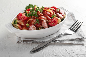 Delicious pasta with sausage and sauce in ceramic dish on light table