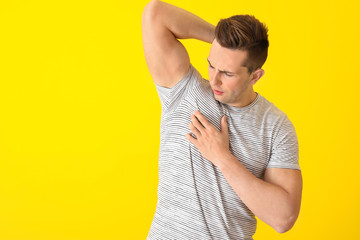 Handsome young man feeling smell of sweat on color background. Concept of using deodorant