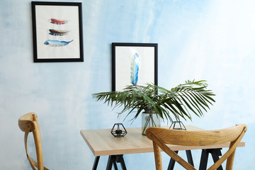 Vase with green tropical leaves on wooden table near light wall