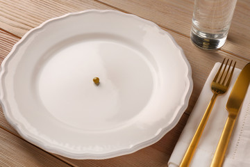 Plate with small peas and cutlery on wooden table. Diet concept