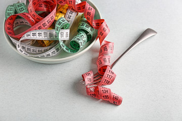 Fork and plate with measuring tapes on light background. Diet concept