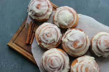 Beautiful fresh cinnamon rolls close-up on wooden grunge texture table. Fragrant homemade cakes, Cinnabon. A Cup of tea on a white saucer, cinnamon sticks. Delicious Breakfast buffet.
