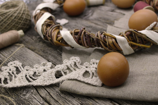Easter composition on wooden background. Preparation for the holiday. Handmade crochet lace, homemade chicken egg, natural wreath from vine branches, linen fabric. Cozy rustic, country style.