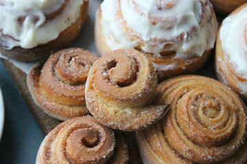 Beautiful fresh cinnamon rolls close-up on wooden grunge texture table. Fragrant homemade cakes, Cinnabon. A Cup of tea on a white saucer, cinnamon sticks. Delicious Breakfast buffet.
