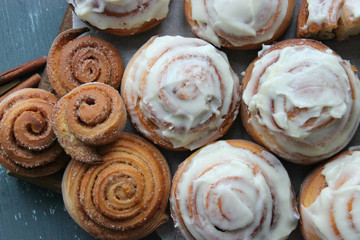 Fototapeta premium Beautiful fresh cinnamon rolls close-up on wooden grunge texture table. Fragrant homemade cakes, Cinnabon. A Cup of tea on a white saucer, cinnamon sticks. Delicious Breakfast buffet.