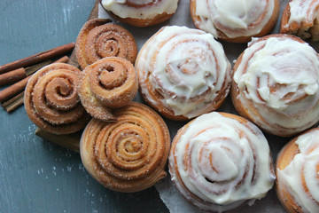 Beautiful fresh cinnamon rolls close-up on wooden grunge texture table. Fragrant homemade cakes, Cinnabon. A Cup of tea on a white saucer, cinnamon sticks. Delicious Breakfast buffet.