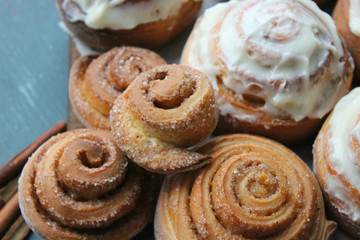 Beautiful fresh cinnamon rolls close-up on wooden grunge texture table. Fragrant homemade cakes, Cinnabon. A Cup of tea on a white saucer, cinnamon sticks. Delicious Breakfast buffet.