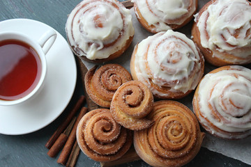 Beautiful fresh cinnamon rolls close-up on wooden grunge texture table. Fragrant homemade cakes, Cinnabon. A Cup of tea on a white saucer, cinnamon sticks. Delicious Breakfast buffet.