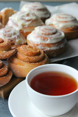 Beautiful fresh cinnamon rolls close-up on wooden grunge texture table. Fragrant homemade cakes, Cinnabon. A Cup of tea on a white saucer, cinnamon sticks. Delicious Breakfast buffet.