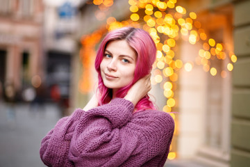 portrait of beautiful young girl with pink hair and purple sweater on city lights background.