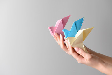 Female hands with origami birds on light background