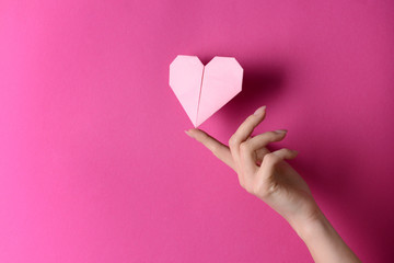 Female hand with origami heart on color background