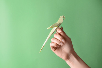 Female hand with origami parrot on color background - obrazy, fototapety, plakaty