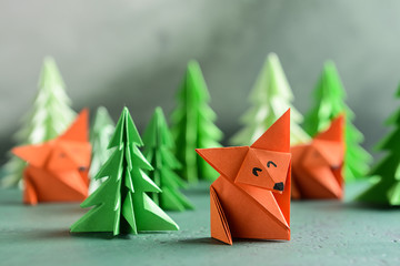 Origami foxes with fir trees on color table - obrazy, fototapety, plakaty