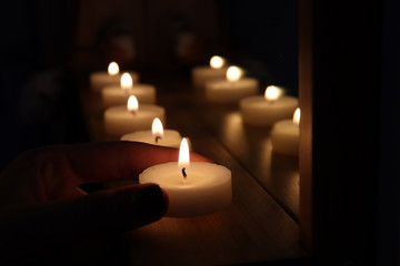 Woman putting burning candles on table in darkness, closeup