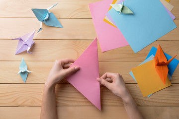 Young woman making origami on wooden table - obrazy, fototapety, plakaty