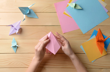 Young woman making origami on wooden table - obrazy, fototapety, plakaty