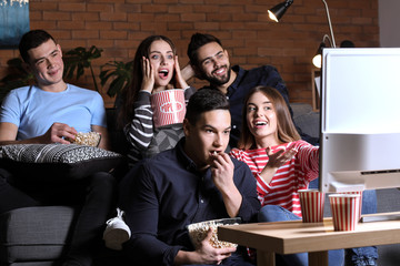 Friends watching TV and eating popcorn at home