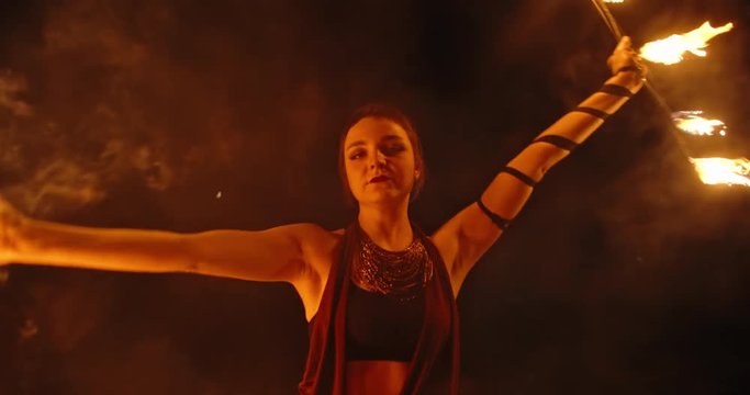 Cool female fire show stuntsman performing, swinging her burning fans - slow motion 4k