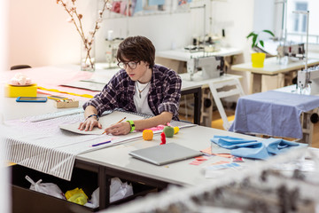 Young dark-haired asian designer with a green watch working in a studio