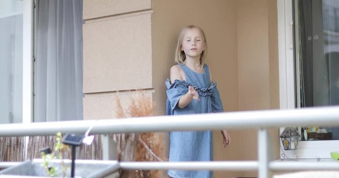 A nice blond girl is standing on the balcony and sending an air kiss.