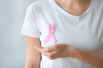 Woman with pink ribbon on light background, closeup. Breast cancer awareness concept