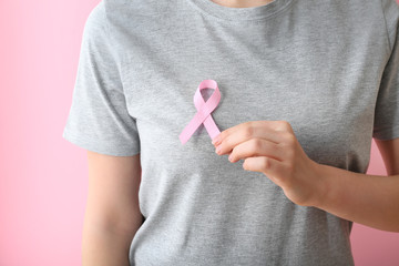 Woman with pink ribbon on color background, closeup. Breast cancer awareness concept