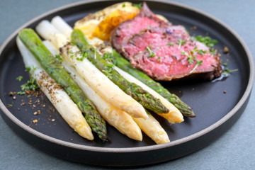 Traditioneller weißer und grüner Spargel mit  barbecue dry aged Rinderfilet und Bratkartoffel serviert als closeup auf einem Modern Design Teller