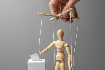 Puppeteer manipulates the doll. Voting is dishonest. The man lowers paper ballet box to put it on...
