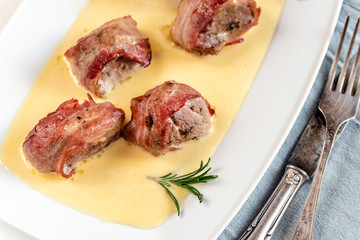 Baked pork tenderloin wrapped in bacon and served in a cheese sauce with rosemary