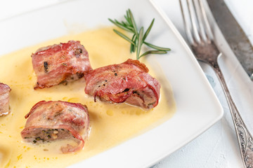 Baked pork tenderloin wrapped in bacon and served in a cheese sauce with rosemary