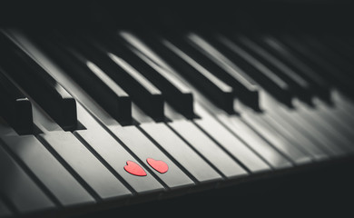 Naklejka premium Two small red hearts on the keyboard of classic piano close up. Concept of love and romantic music