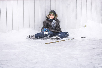 Kid boy hockey player having a rest on ice after playing hockey period on street skating rink during winter holidays