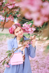 Fototapeta premium Beautiful girl with pink hair in a fashionable blue pantsuit standing next to colorful flowers.