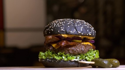 An appetizing black hamburger on a wooden board with fresh vegetables.