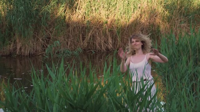 Positive and funny video, an adult girl with blond curly hair is fun and defiantly dancing in the reeds and green grass, fooling around like a child. bright and colorful video, a sense of childhood
