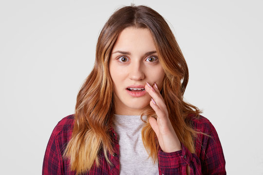 Headshot of surprised young woman looks with astonishment, has wavy hair, scared of something horrified, has appealing appearance, models against white background. Facial expressions concept