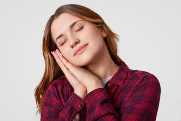 Photo of attractive woman takes nap, leans on hands, has eyes closed, dressed in casual clothes, isolated over white background, being tired, wants to sleep. People, sleeping, tiredness concept