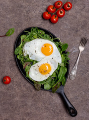 Fried eggs on pan with herbs and cherry tomatoes on brown background