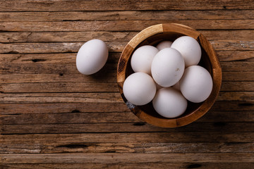 Over head photograph of a wooden bowl of fresh chicken eggs on a wood board