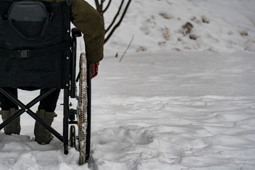 Disabled handicapped man has a hope. He sits in a wheelchair and looks at a mountain of snow. The complexity of the movement of the disabled. On a wheelchair in the winter.