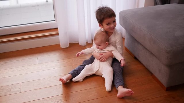 Little brother sit hug his baby sister children play at home