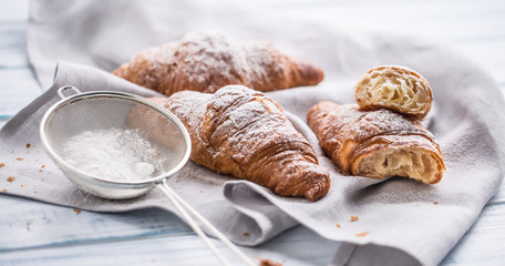Fresh buttery croissants sprinkled with sugar powder on kitchen table.