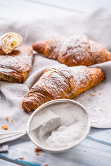 Fresh buttery croissants sprinkled with sugar powder on kitchen table.
