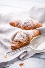 Fresh buttery croissants sprinkled with sugar powder on kitchen table.