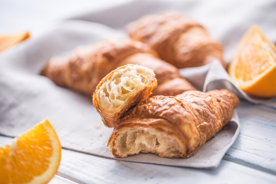 Fresh buttery croisants with sweet oranges on kitchen napkin.