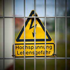 Schild mit der Aufschrift "Hochspannung Lebensgefahr" an einem Zaun