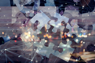 Business people join puzzle pieces in office. Concept of teamwork and partnership. double exposure...